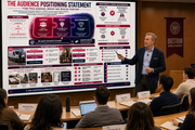 Person giving a presentation in front of an audience with a large screen displaying an audience positioning statement.